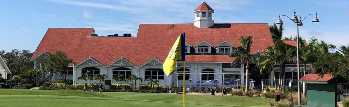The historic red-roofed clubhouse at Fort Myers Country Club behind a putting green and flag